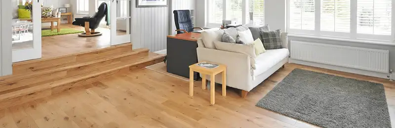 A modern living room with professionally installed laminate flooring, a beige sofa, a small side table, a gray rug, and large windows with white shutters in Columbia, MO
